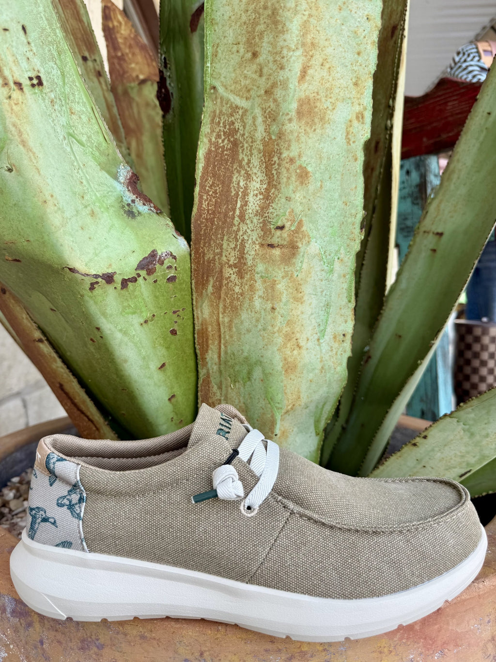 Men's tan woven-textile slip-on shoe with a green duck-print heel panel, white elasticized laces, stitched moc toe, and white foam sole — Blair's Western Wear Marble Falls TX