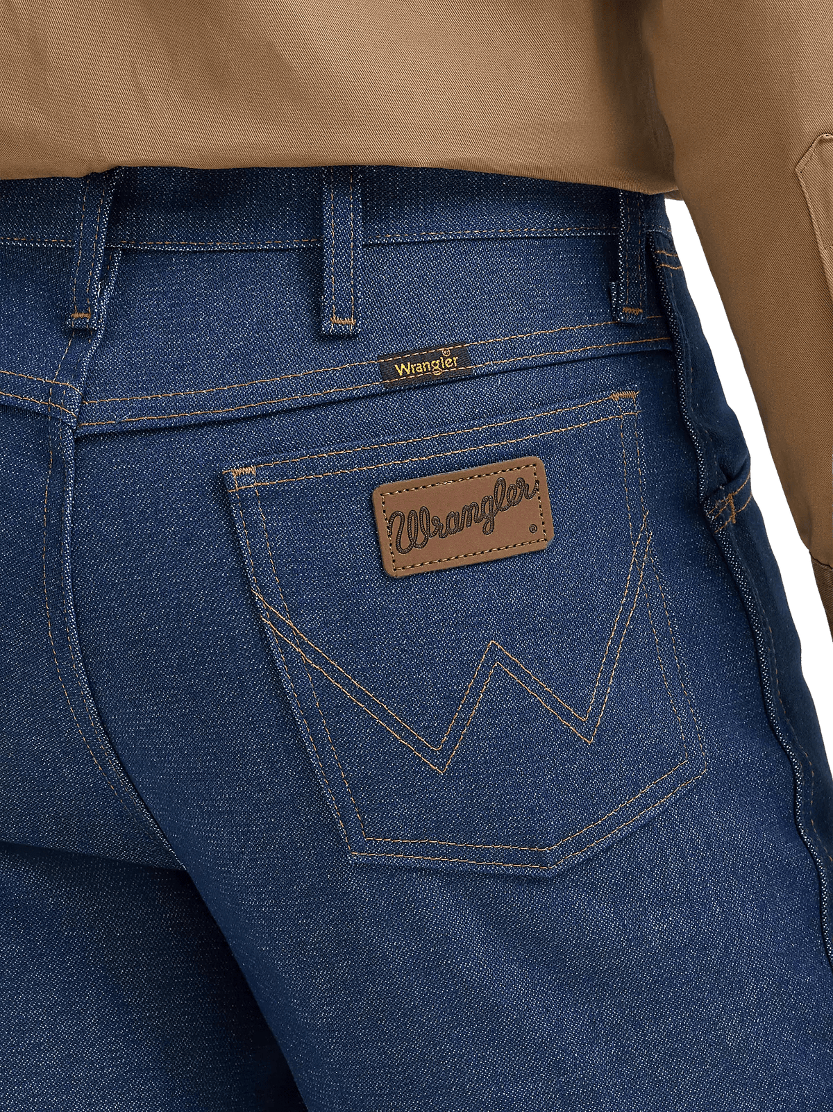 Close-up of the back waistband and pocket area of blue denim jeans, showing a brown leather Wrangler patch on the back pocket and a small yellow Wrangler tab near the waistband, with tan fabric at the top.