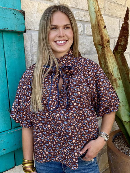 Women's brown ditsy floral print top with denim-trimmed tie neck bow detail close-up — Blair's Western Wear Marble Falls TX