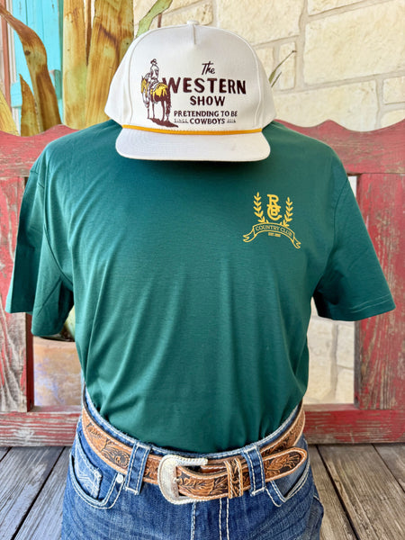 Men's hunter green Raised by Coyote Coyote Country Club short sleeve tee with gold RBC monogram chest logo, front view styled with jeans and tooled leather belt — Blair's Western Wear Marble Falls TX