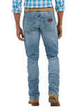 Rear view of a person wearing light blue denim jeans with a brown leather patch on the back pocket, a tan belt, and brown boots against a white studio background.