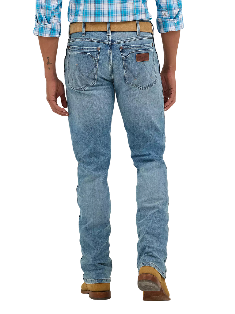 Rear view of a person wearing light blue denim jeans with a brown leather patch on the back pocket, a tan belt, and brown boots against a white studio background.