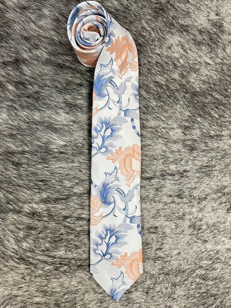 A rolled-up necktie with a white base and a watercolor-style floral pattern in blue and peach, laid flat on a gray faux fur background.