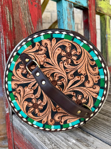 American Darling round makeup case in natural and black hair-on hide with tooled leather floral front, structured round shape, and full zipper closure – ADBGA317. Available at Blair's Western Wear, Marble Falls, TX.