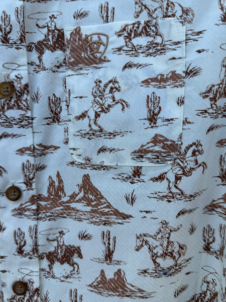 Close up of Boy's Long Sleeve Ariat Western Desert Shirt - 10062392. This white button down shirt features a fun western desert graphic with cowboys riding horses in the wild and it also has a pocket on the left side of the chest. Available at Blair's Western Wear located in Marble Falls. TX