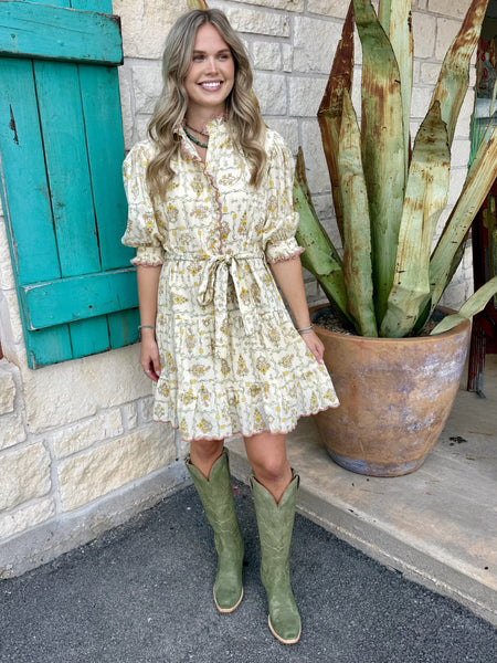 Women's cream floral block print mini dress with ruffle collar, puff sleeves, tie waist, tiered skirt, and ricrac scallop hem styled with western boots — Blair's Western Wear Marble Falls TX