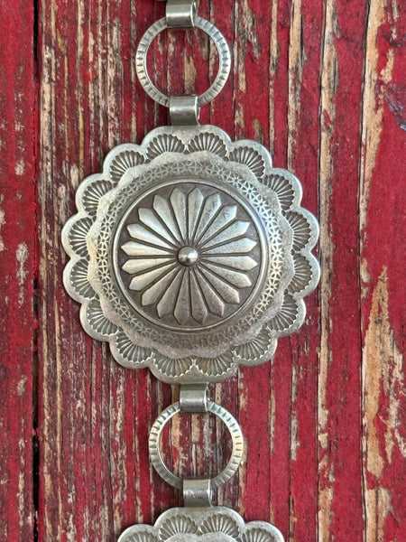 Stacked round silver conchos with deeply stamped sunburst and floral engraving, linked by open rings — this belt carries the weight of real Western artistry. The scalloped edges and layered detailing give it a heritage feel that pairs effortlessly with everything from denim to dresses