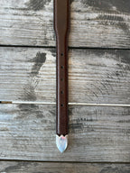 A brown leather belt with a silver-toned western-style buckle and decorative tip, coiled on a rustic wooden surface with a distressed red wooden background.