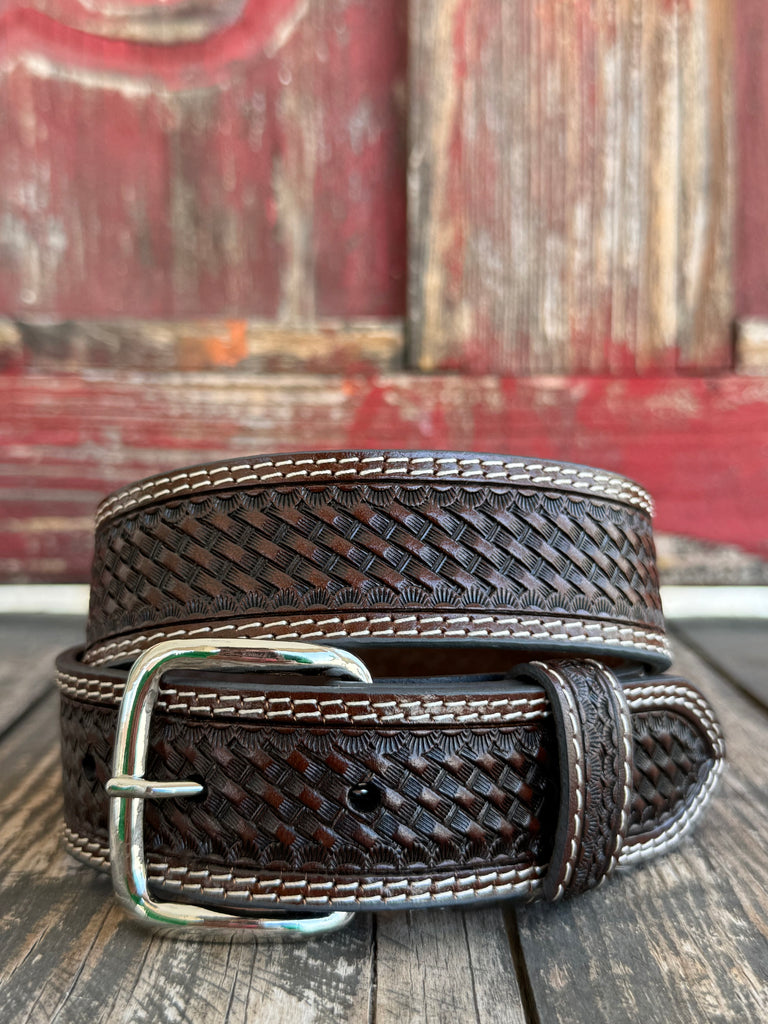 A dark brown woven leather belt with a silver buckle, coiled on a rustic wooden surface with a weathered red wooden background. Available at Blair's Western Wear located in Marble Falls TX