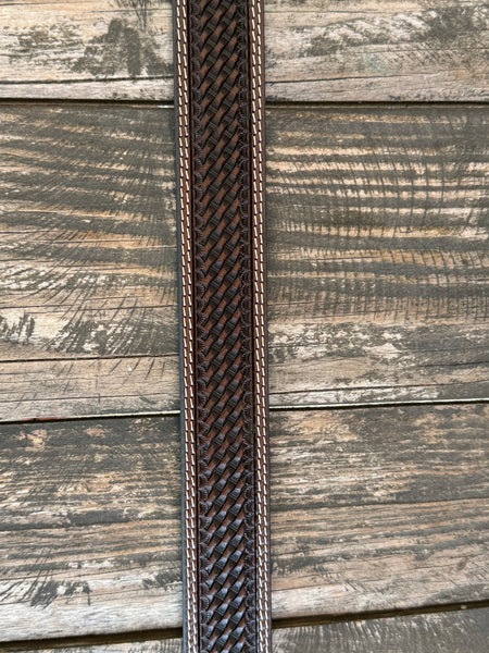 A dark brown woven leather belt with a silver buckle, coiled on a rustic wooden surface with a weathered red wooden background. Available at Blair's Western Wear located in Marble Falls TX