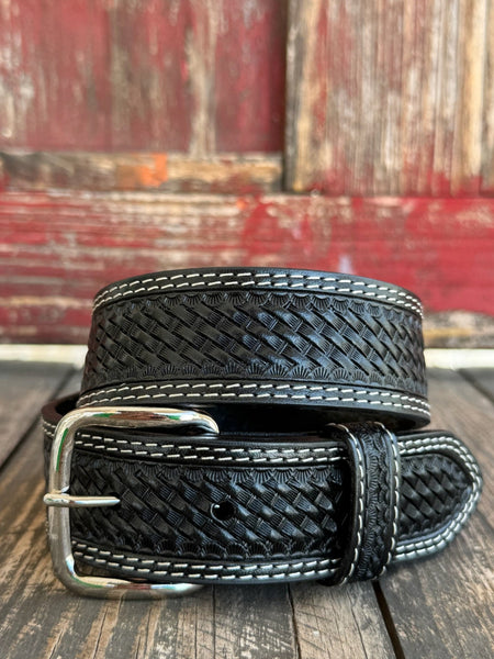 A black woven leather belt with white contrast stitching and a silver buckle, coiled on a rustic wooden surface with a weathered red wooden background. Available at Blair's Western Wear, Marble Falls, TX