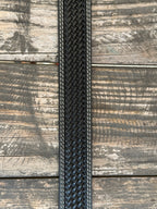 A close-up of a black woven leather belt, featuring white contrast stitching , laid flat on a rustic wooden plank background. Available at Blair's Western Wear, Marble Falls, TX