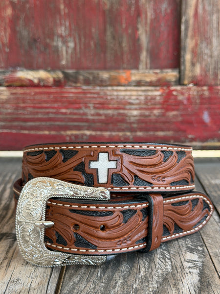 Two-toned brown and black tooled leather features sweeping floral scrollwork and a standout white hair-on-hide cross inlay, finished with cream stitching and an engraved silver buckle — bold western faith and craftsmanship in one. Available at BLAIR'S Western Wear located in Marble Falls TX 