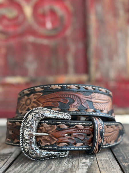 Rich brown leather is hand-tooled with intricate floral and leaf patterns, edged in black with laced detailing and finished with a bold engraved silver buckle — a classic western belt crafted with real artisan character. Available at BLAIR'S Western Wear located in Marble Falls TX 