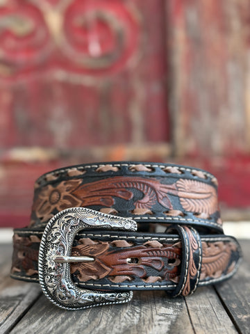 Rich brown leather is hand-tooled with intricate floral and leaf patterns, edged in black with laced detailing and finished with a bold engraved silver buckle — a classic western belt crafted with real artisan character. Available at BLAIR'S Western Wear located in Marble Falls TX 