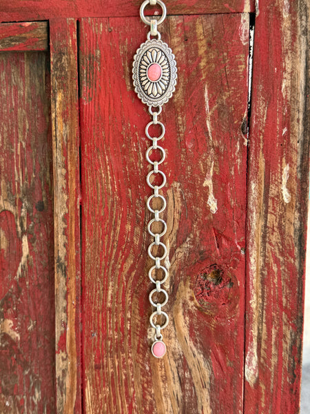 A1308230 — Kid's Pink Concho Chain Western Belt Full silver concho chain belt with repeating oval silver conchos featuring engraved petal/sunburst detail, rope edge border, and pink stone center in each. Silver O-ring links connect each concho. Adjustable silver O-ring chain tail with small pink stone drop tip. Available at Blair's Western Wear located in Marble Falls TX 