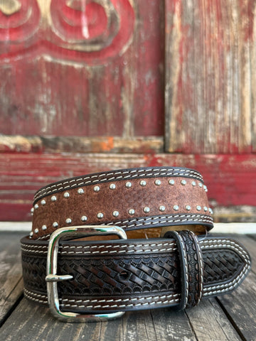 Western belt featuring a dark brown hand-tooled basketweave pattern with contrasting white stitching. The center is accented with distressed brown leather and two rows of antique silver studs for added detail. It also features 2 Praying Cowboy Stud Conchos. Finished with a polished silver roller buckle and matching leather keeper, this belt is built for durable everyday wear.Available at Blair's Western Wear, Marble Falls, TX

