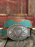 Warm tan leather is painted with a bold turquoise floral vine pattern and paired with a large oval engraved silver buckle featuring a scrollwork heart center — Available at BLAIR'S Western Wear located in Marble Falls TX 
