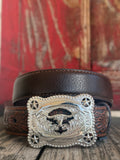 A dark brown leather belt with a highly detailed, engraved silver buckle featuring a western bull skull and star motifs, displayed on a rustic wooden surface with a red wooden background. Available at Blair's Western Wear located in Marble Falls TX