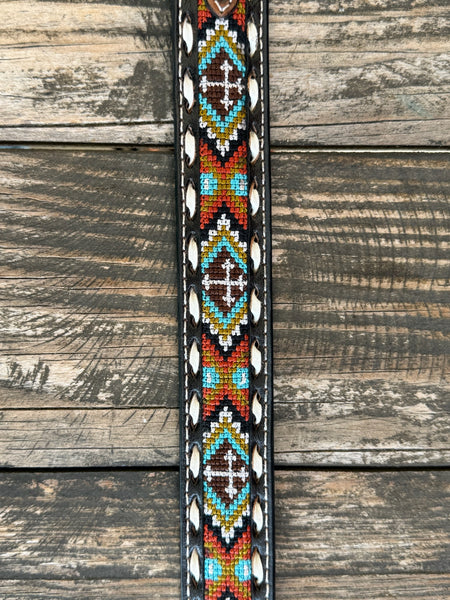 Kid's Aztec-Inspired Embroidered Cross Belt Black leather strap with a multicolor Aztec-inspired embroidered cross panel in teal, orange/red, olive/gold, and white. White lace whipstitch edge detail flanks the embroidered panel. Cognac floral scroll-tooled leather keeper loop. Large oval silver buckle with 3D bucking bronco and rider centerpiece, ornate floral scroll engraving, and beaded rope border. Available at Blair's Western Wear, Marble Falls, TX