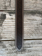 A dark brown woven leather belt with a silver buckle, coiled on a rustic wooden surface with a weathered red wooden background. Available at Blair's Western Wear located in Marble Falls TX