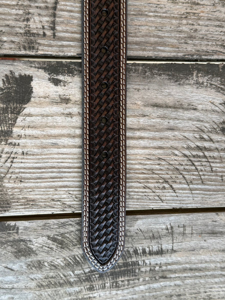 A dark brown woven leather belt with a silver buckle, coiled on a rustic wooden surface with a weathered red wooden background. Available at Blair's Western Wear located in Marble Falls TX