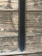 A close-up of a black woven leather belt, featuring white contrast stitching , laid flat on a rustic wooden plank background. Available at Blair's Western Wear, Marble Falls, TX