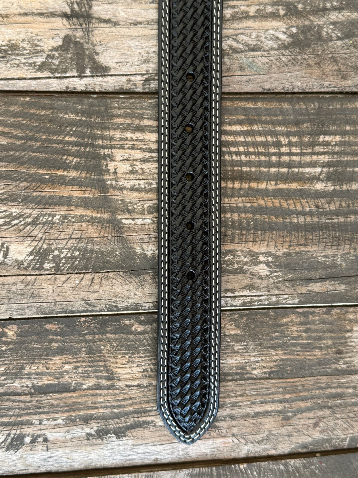 A close-up of a black woven leather belt, featuring white contrast stitching , laid flat on a rustic wooden plank background. Available at Blair's Western Wear, Marble Falls, TX