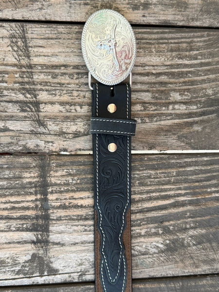 A western-style leather belt coiled on a rustic wooden surface, featuring a large engraved silver buckle with a steer design, a dark brown leather strap, and a black leather section with white stitching and a small diamond-shaped logo. It also features longhorn cutouts. Available at BALIR'S Western Wear located in Marble Falls TX 