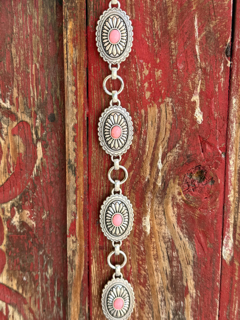 A1308230 — Kid's Pink Concho Chain Western Belt Full silver concho chain belt with repeating oval silver conchos featuring engraved petal/sunburst detail, rope edge border, and pink stone center in each. Silver O-ring links connect each concho. Adjustable silver O-ring chain tail with small pink stone drop tip. Available at Blair's Western Wear located in Marble Falls TX 