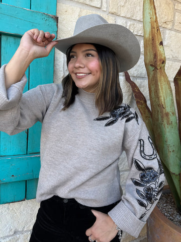 Cozy meets chic in this Ariat knit sweater, featuring a warm tan base with striking black floral embellishments along the shoulder and sleeve. Its mock-neck design, ribbed details, and relaxed fit make it the perfect blend of comfort and style for any season. Available at BLAIR'S Western Wear located in Marble Falls TX.
