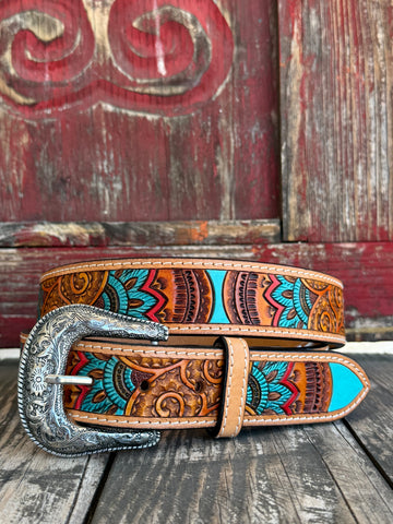 Natural tan leather hand-tooled with flowing floral scrollwork and vibrant Aztec-inspired hand-painted color — turquoise, coral, orange, purple, and gold — finished with an ornate silver floral scroll buckle. Shop at Blair's Western Wear — blairswesternwear.com.

