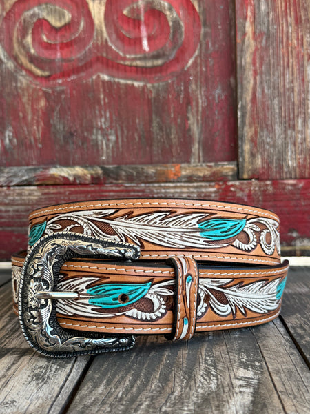 A tooled brown leather belt with turquoise and white feather designs, featuring an ornate silver buckle, displayed on a rustic wooden surface in front of a weathered red wooden door.