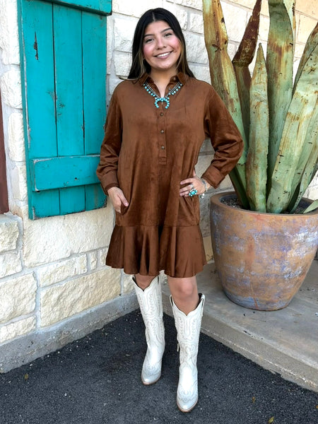 This Ivy Jane Suede Shirtdress in chestnut blends classic western charm with soft, everyday comfort. Made from rich faux suede, it features a collared neckline, button-front detail, a relaxed fit, and a flirty ruffle hem. With convenient pockets and a warm, earthy tone, it’s the perfect piece for effortless fall styling. Available at BLAIR's Western Wear located in Marble Falls, TX. 