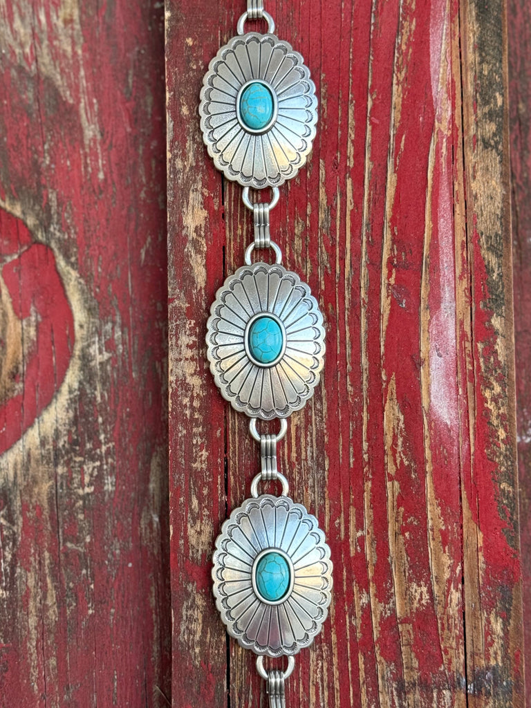 A fully linked silver concho chain belt featuring large oval conchos with intricate stamped sunburst detailing and a vibrant turquoise center stone in each — connected by silver rings throughout for an adjustable, flexible fit - timeless, southwestern-inspired western belt that adds instant color and character to jeans, dresses, or tunics.