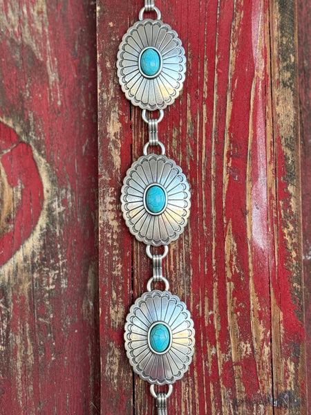 A fully linked silver concho chain belt featuring large oval conchos with intricate stamped sunburst detailing and a vibrant turquoise center stone in each — connected by silver rings throughout for an adjustable, flexible fit - timeless, southwestern-inspired western belt that adds instant color and character to jeans, dresses, or tunics.