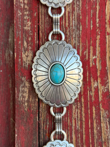 A fully linked silver concho chain belt featuring large oval conchos with intricate stamped sunburst detailing and a vibrant turquoise center stone in each — connected by silver rings throughout for an adjustable, flexible fit - timeless, southwestern-inspired western belt that adds instant color and character to jeans, dresses, or tunics.