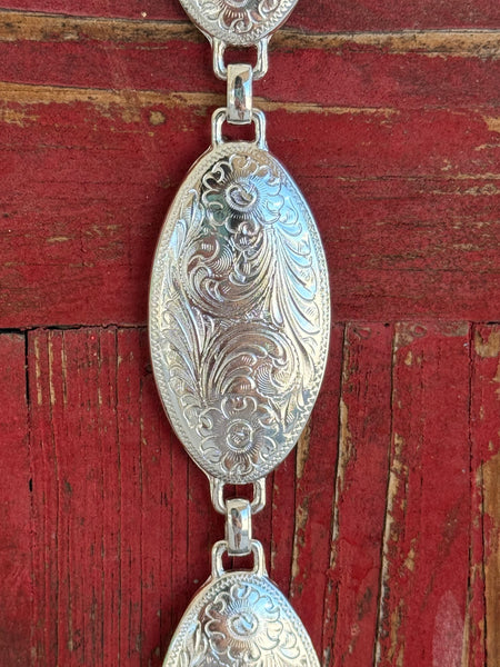 A fully linked silver concho chain belt featuring large oval conchos with intricate etched scroll and floral engraving throughout, connected by silver rings for an adjustable, flexible fit. All-silver, all-Western, and effortlessly elegant. Shop at Blair's Western Wear — blairswesternwear.com.