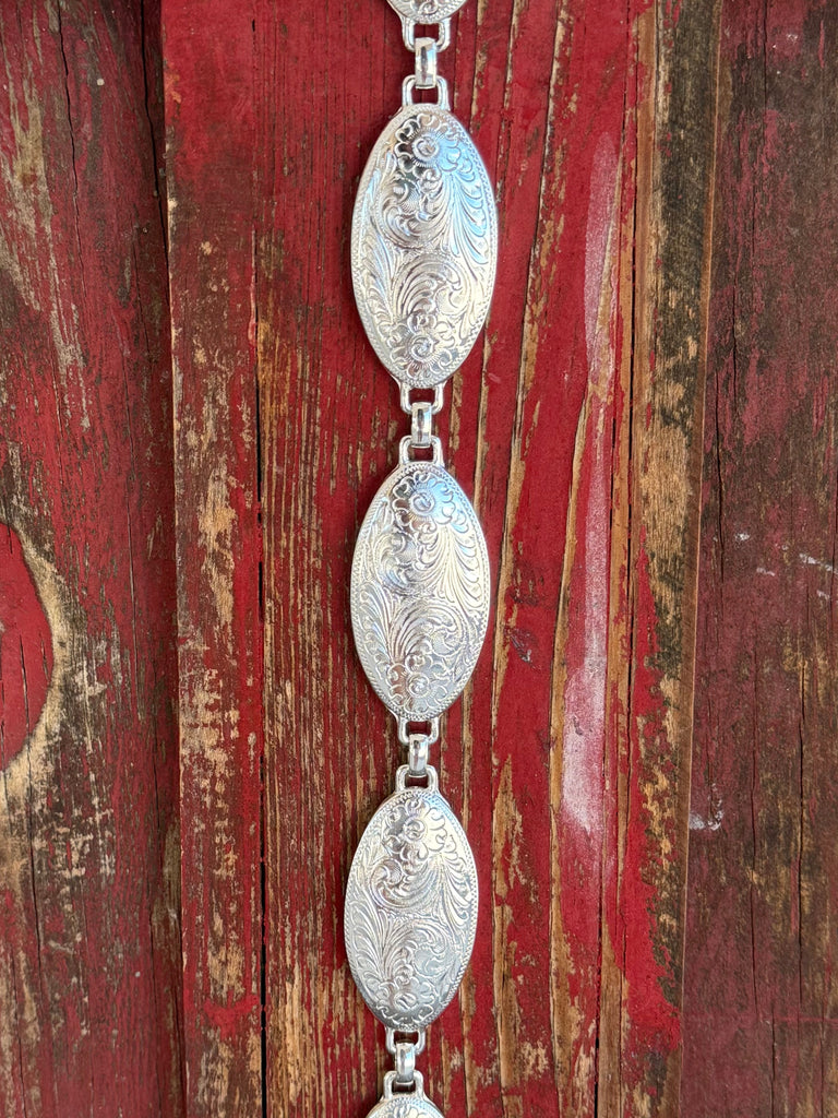 A fully linked silver concho chain belt featuring large oval conchos with intricate etched scroll and floral engraving throughout, connected by silver rings for an adjustable, flexible fit. All-silver, all-Western, and effortlessly elegant. Shop at Blair's Western Wear — blairswesternwear.com.