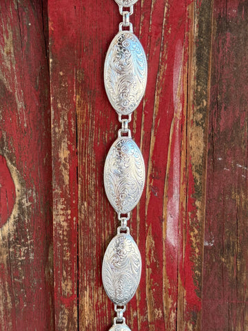 A fully linked silver concho chain belt featuring large oval conchos with intricate etched scroll and floral engraving throughout, connected by silver rings for an adjustable, flexible fit. All-silver, all-Western, and effortlessly elegant. Shop at Blair's Western Wear — blairswesternwear.com.