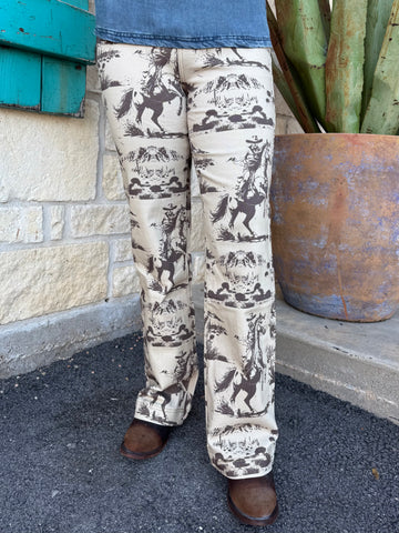 These Lucky & Blessed Western Print Trousers bring vintage cowboy vibes to any outfit. Made with a soft, lightweight fabric and a comfortable mid-rise fit, they feature an all-over brown rodeo scene print on a cream background. Finished with a flattering bootcut leg, these trousers pair perfectly with your favorite denim tops, graphic tees, or boots for an effortless western look. Available at BLAIR'S Western Wear located in Marble Falls TX.
