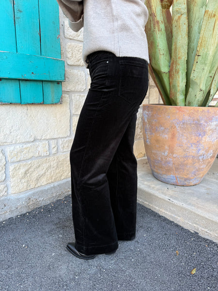 Women’s black corduroy trousers with a mid-rise waist with belt loops, a classic button-and-zip closure, and straight wide-leg bottoms. The corduroy fabric has a soft, fine-ribbed texture that gives the pants a slightly velvety appearance. Lucky & Blessed Mid-Rise Corduroy Trouser in Black – JE462-BLK - BLAIR'S Western Wear located in Marble Falls TX.