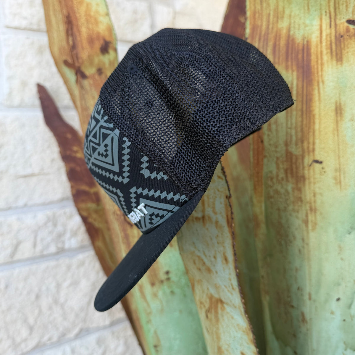 A black trucker-style cap with a gray geometric pattern on the front panel