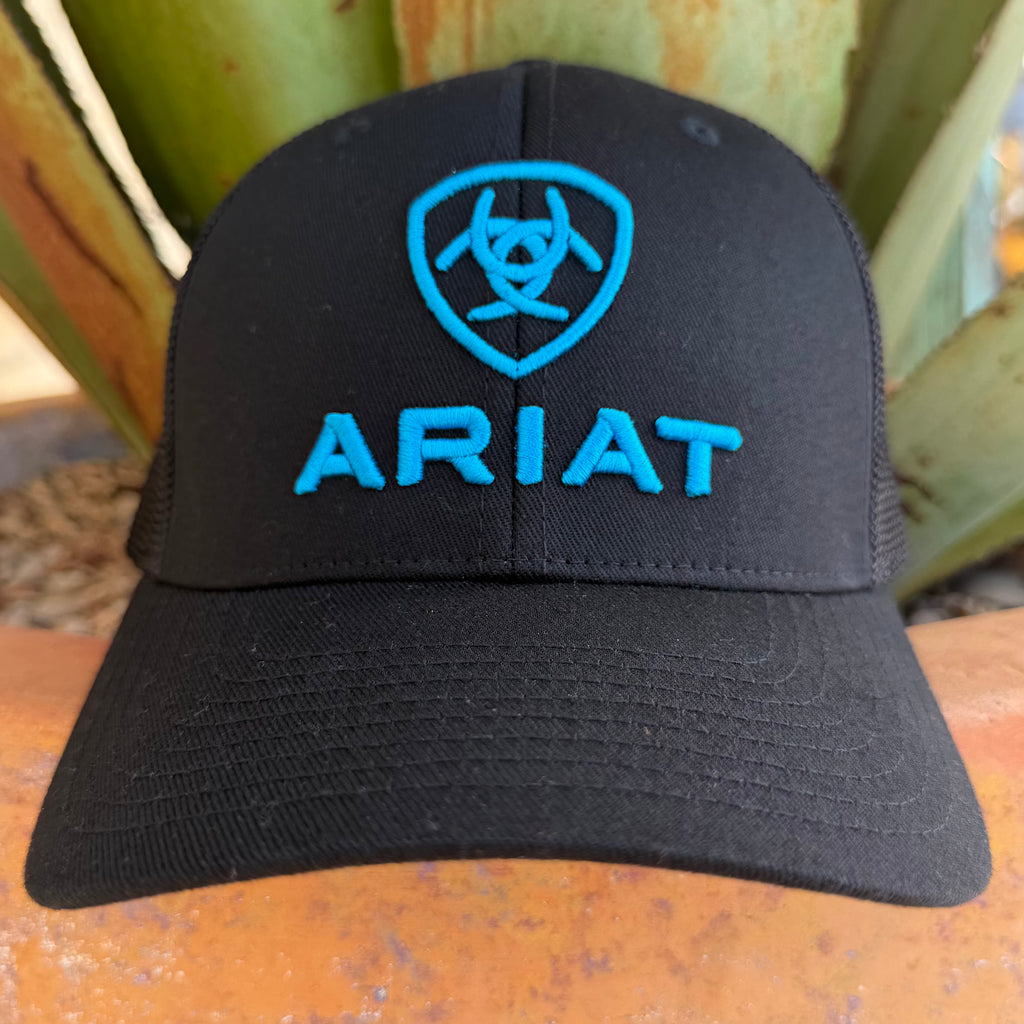 A black trucker-style cap with a bright blue embroidered shield logo and the word 'ARIAT' on the front