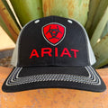 A black and gray trucker-style cap with a red shield logo and the word 'ARIAT' embroidered on the front