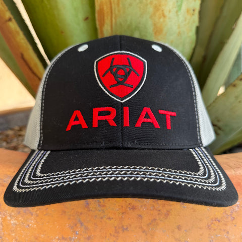 A black and gray trucker-style cap with a red shield logo and the word 'ARIAT' embroidered on the front