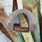 A beige mesh-back trucker hat with a brown adjustable strap and 'ARIAT' embroidered in gold 