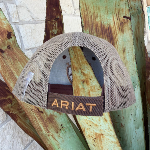 A beige mesh-back trucker hat with a brown adjustable strap and 'ARIAT' embroidered in gold 