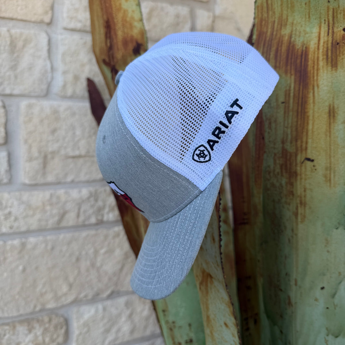 A light gray and white trucker-style cap with the ARIAT logo on the side