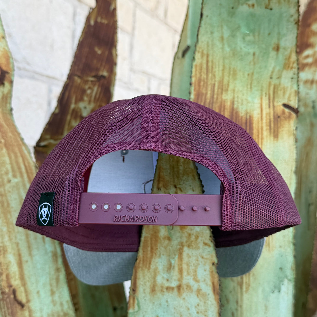 A burgundy mesh trucker hat with a matching adjustable strap and gray visor